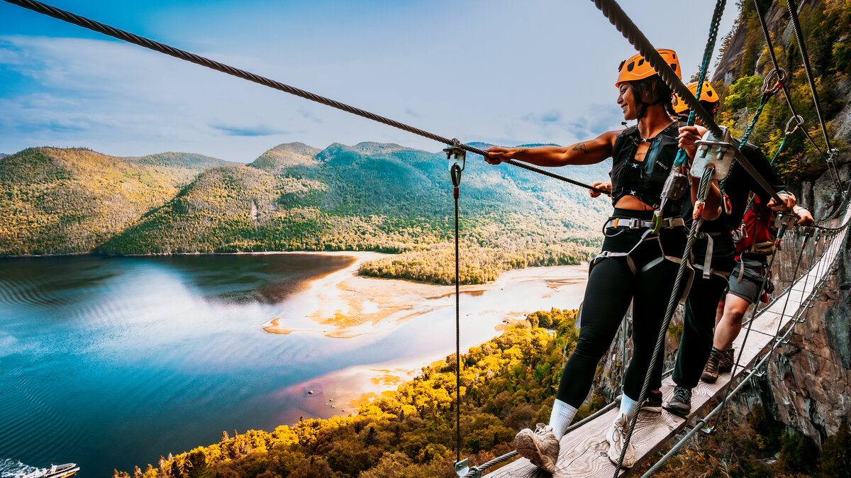 Groupe de jeune sur une passerelle de la Via Ferrata avec le Fjord du Saguenay en arrière plan.