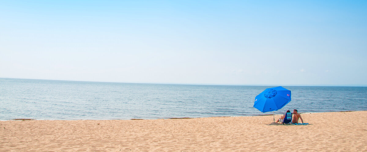 Belle plage avec un ciel bleu et un couple sous un parasol.