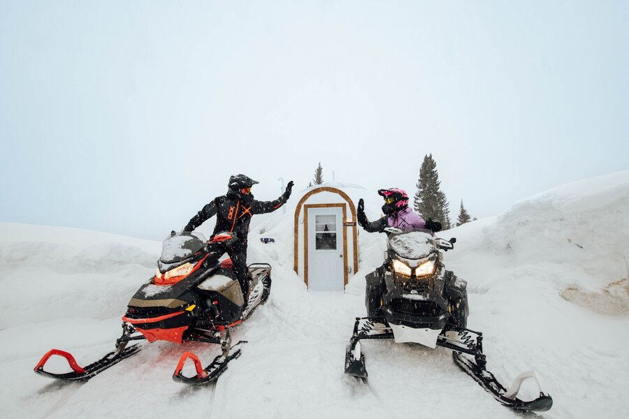 Motoneigistes devant un refuge enneigé en montagne