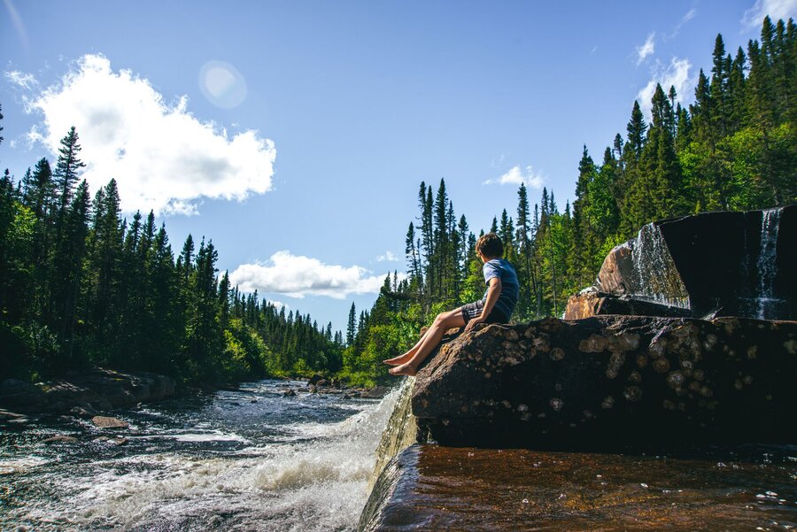 Jeune homme sur le bord d'une rivière en forêt