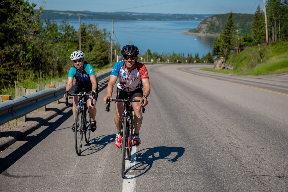 People cycling up a hill with the Saguenay Fjord in the background