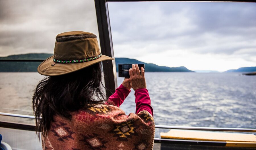Femme de dos qui photographie le fjord du Saguenay avec son cellulaire.
