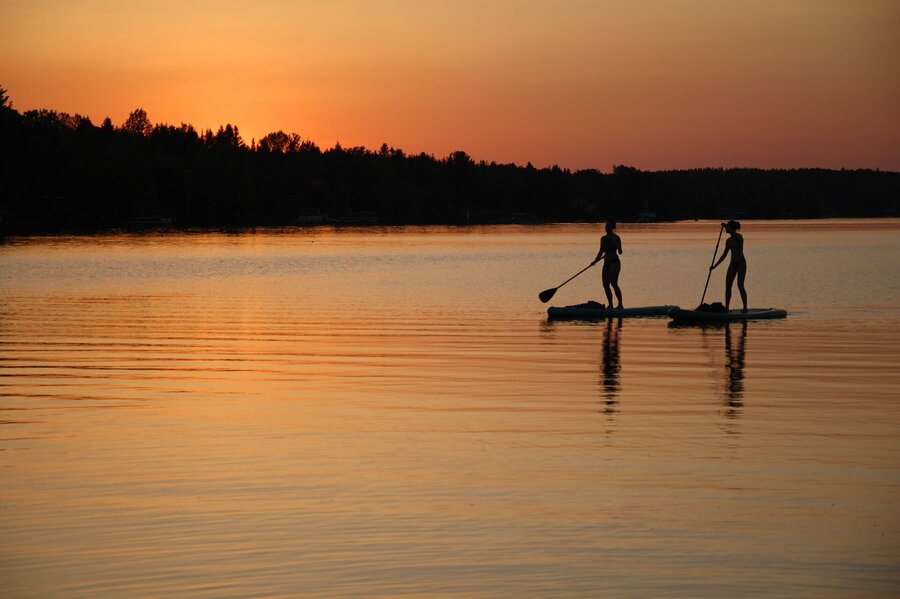 Deux personnes en planche à rame sur l'eau au coucher de soleil.