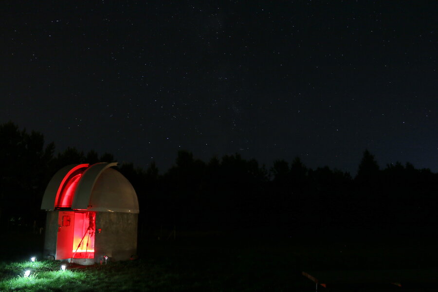 Small astronomical observatory lit up in red at night, under a starry sky