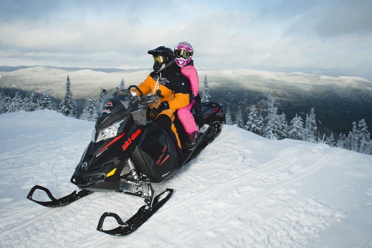 Snowmobiling couple with a view of the Mont-Valin mountains