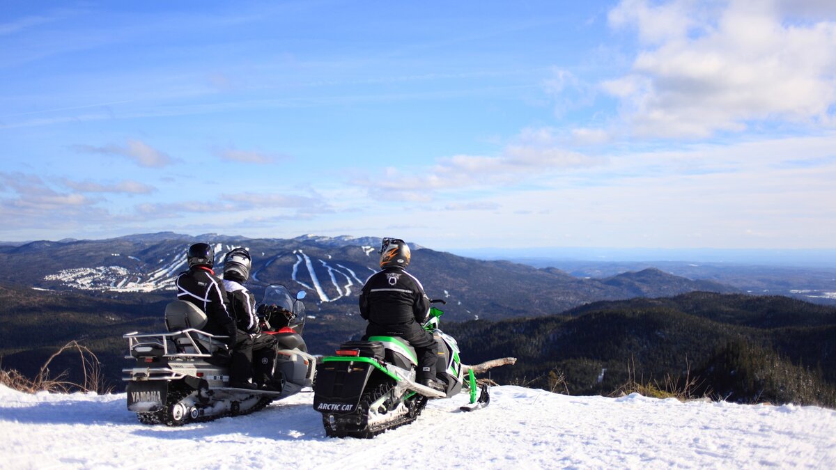 Motoneigiste prenant une pause sur le haut d'une montagne en admirant le paysage